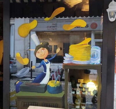 Peinture à la main sur vitrine pour une creperie. La peinture représente une bigouden faisant des crêpes, bretonne (illustration)