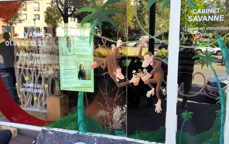 Peinture à la main sur vitrine pour agence immobilière. La peinture représente deux singe en train de trinquer avec des cocktail sur des liannes dans la jungle. vanves 2022