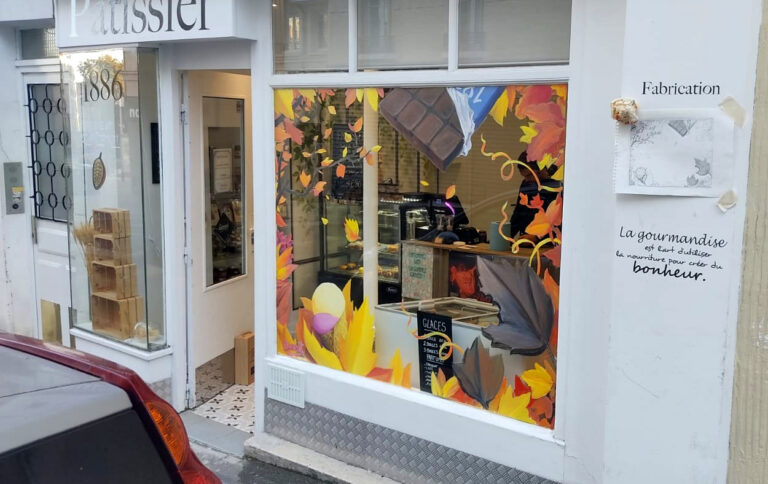 Peinture à la main sur vitrine pour un chocolatier. La peinture représente une décoration automnale avec une plaquette de chocolat et des feulles d'automne. vanves 2022