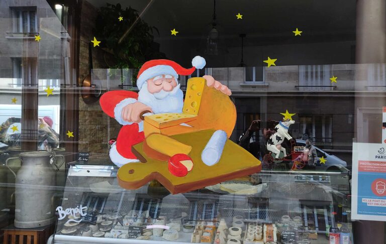 Peinture à la main sur vitrine pour une fromagerie à paris 2021. La peinture représente un pere noel qui découpe du fromage avec un plateau de fromage.