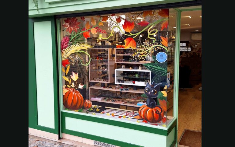 peinture sur vitrine sur le theme de l'automne avec un petit chat des citrouille et de la végétation.