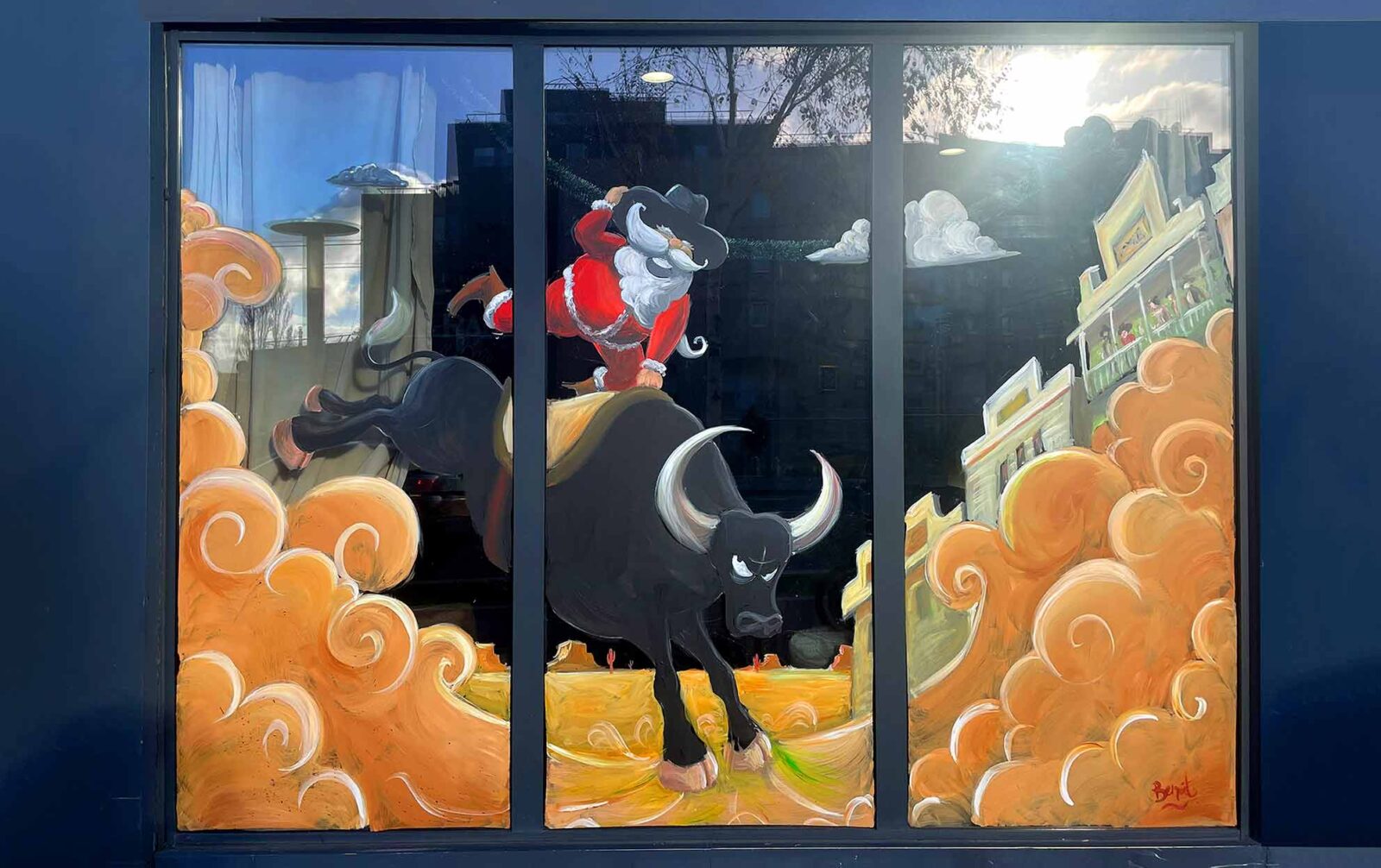 Peinture sur vitrine faite à la main à l'acrylique pour un restaurant à noel. La peinture représente le père Noel chevauchant un taureau dans un village western